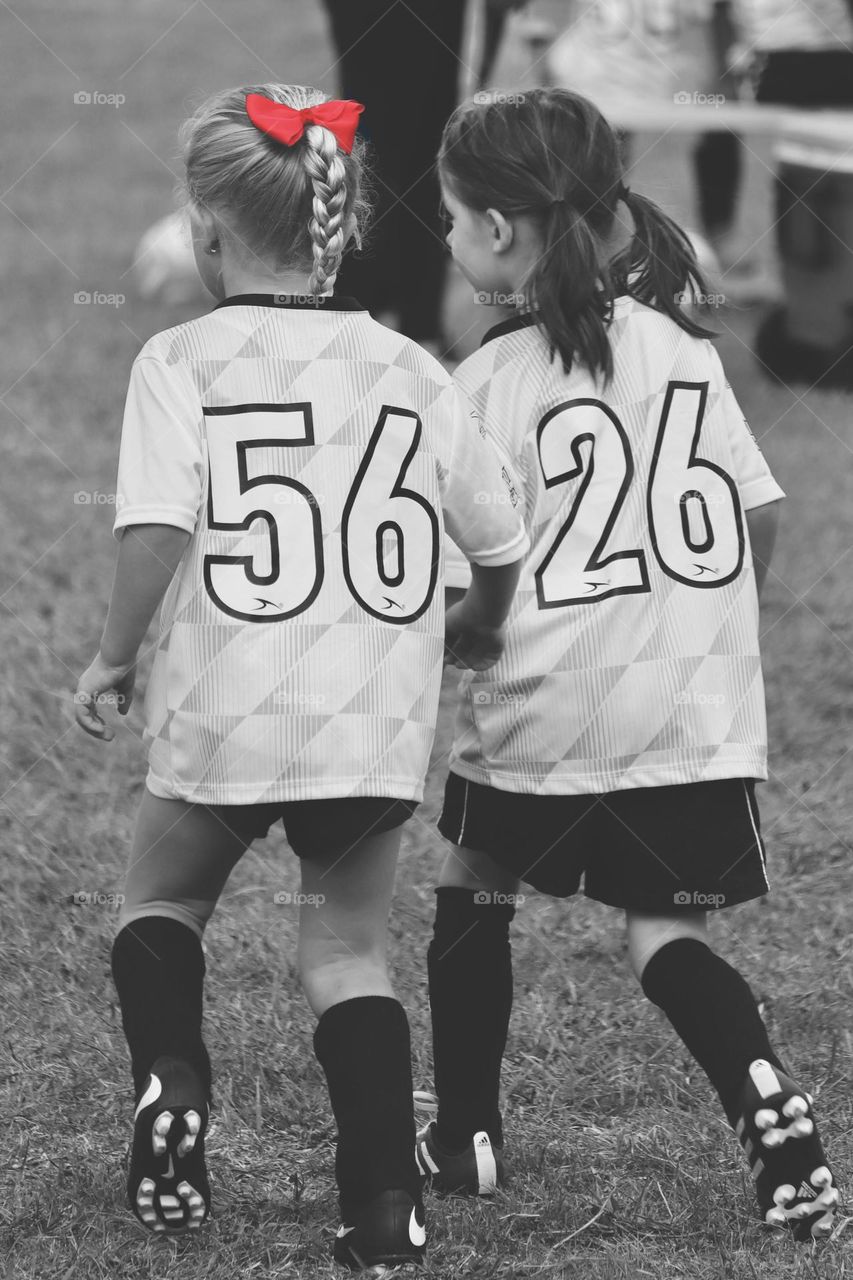 Two young girls playing soccer walk on the field together, bonding over mutual activity 