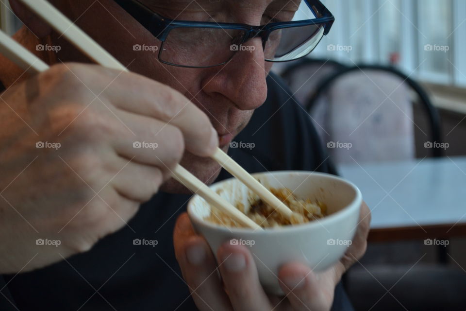 Closeup Caucasian man eating Chinese food with chopsticks from bowl