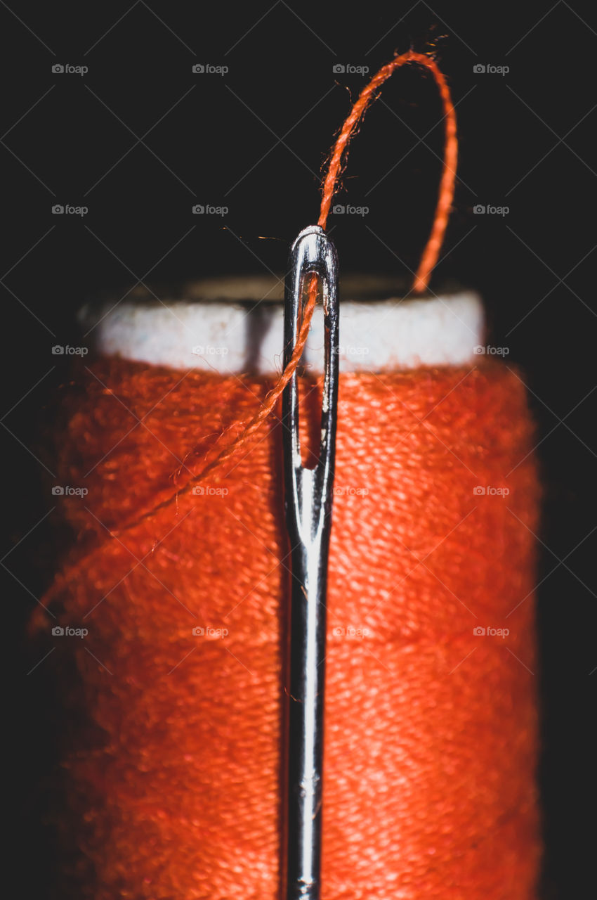 Macro shot of Orange color thread in the tiny hole of needle.