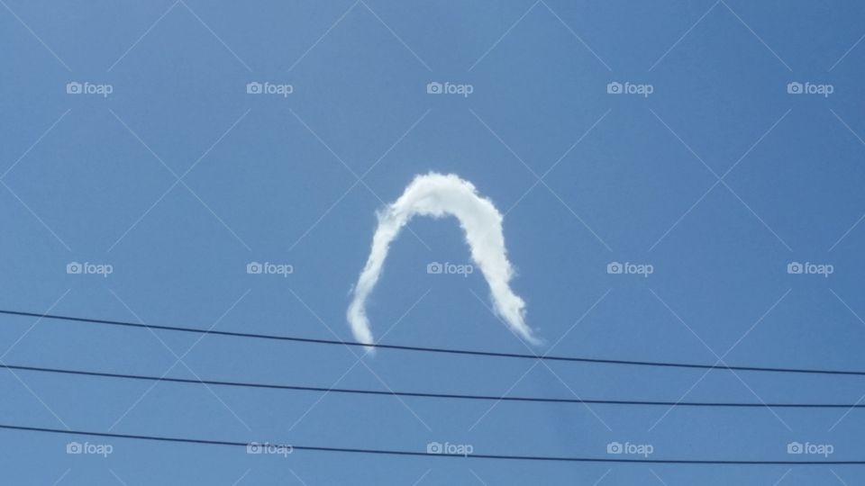 A cloudy formation in the shape of a wig alone in the blue sky next to some power lines.