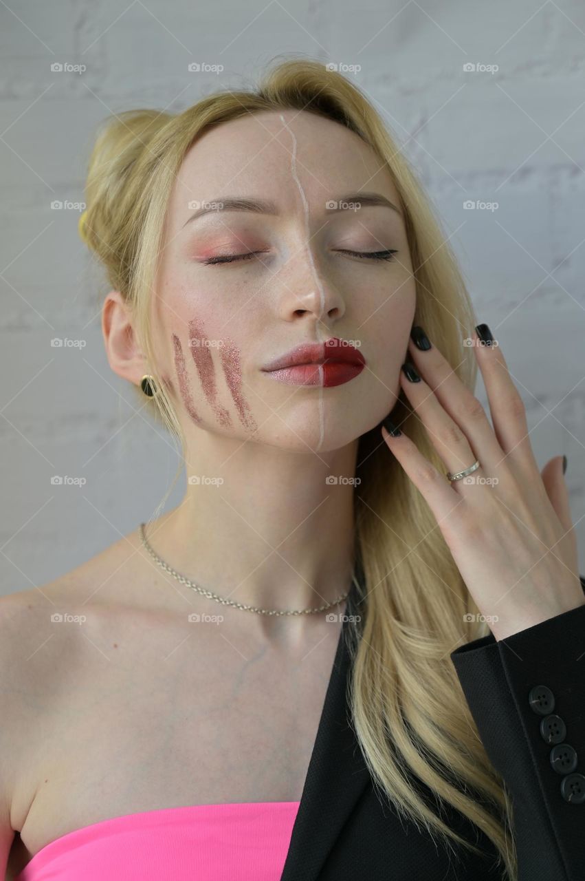 Close-up portrait of a blonde girl with different make-up on half of her face with hand near face on white background