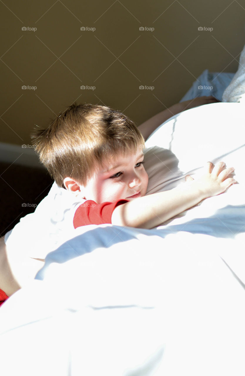 Young boy leaning against a bed with sunlight from a window casting shadows