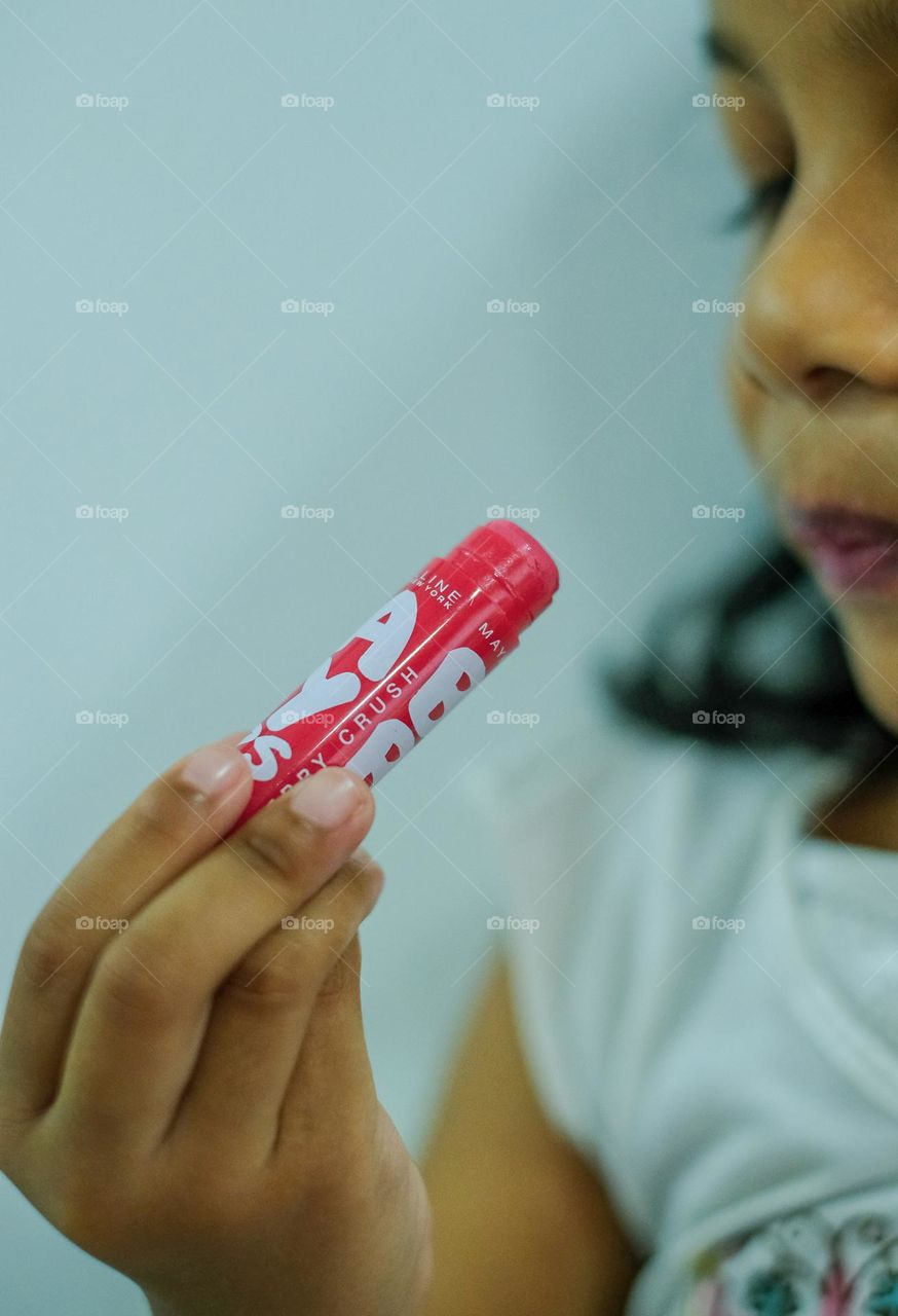 Cropped view of young girl holding lip balm near her lips isolated with dark background.