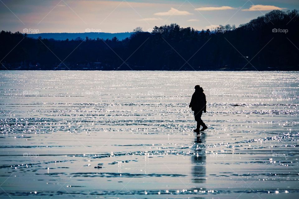 A man walks on a frozen lake to get to his ice fishing hole, making it appear as though he is walking on water.