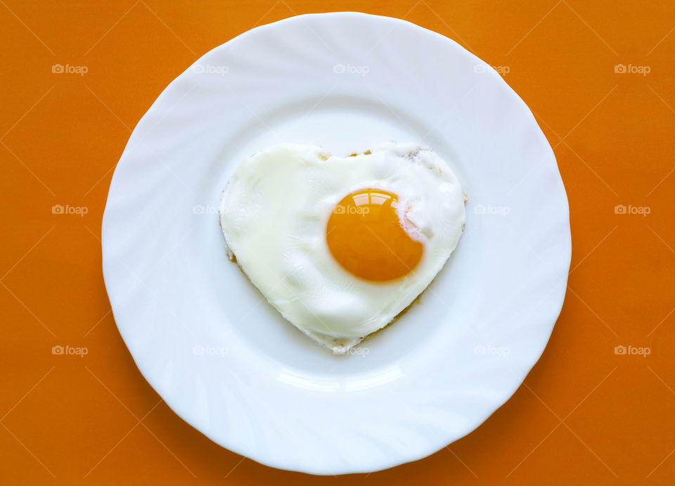 Scrambled eggs. Scrambled eggs in heart shape on white plate and yellow background