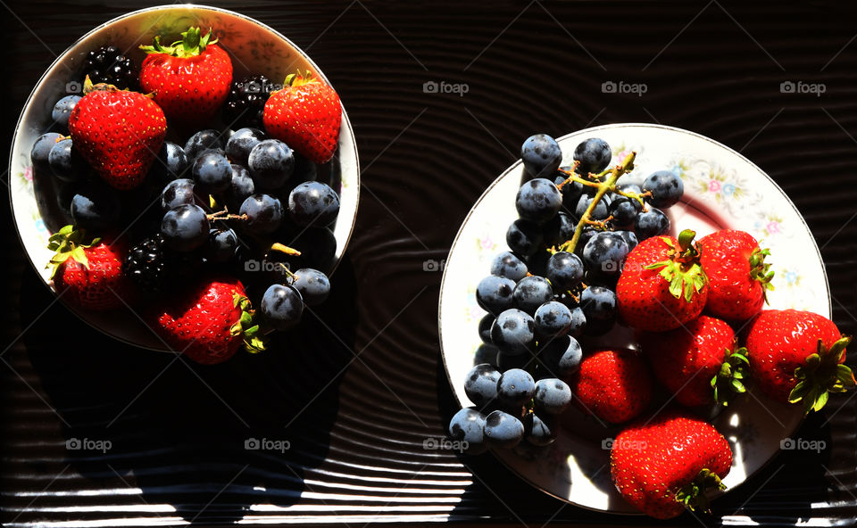 Vibrant fresh and ripe strawberries, blueberries, and blackberries are assorted on white china dishes on a china serving plate.