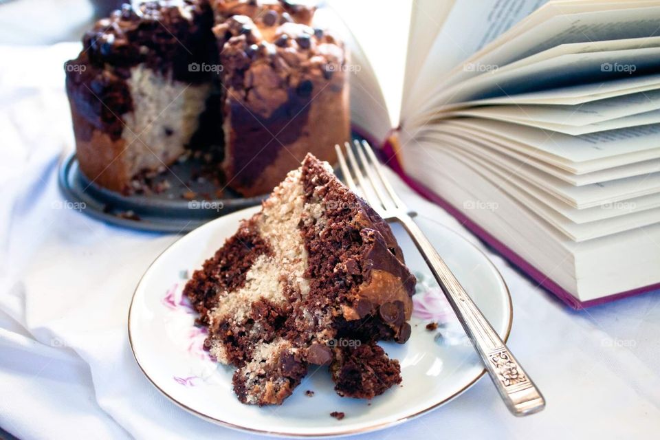 Marble cake on a floral plate, with a silver fork at the side. Background features the full cake as well as an open book.