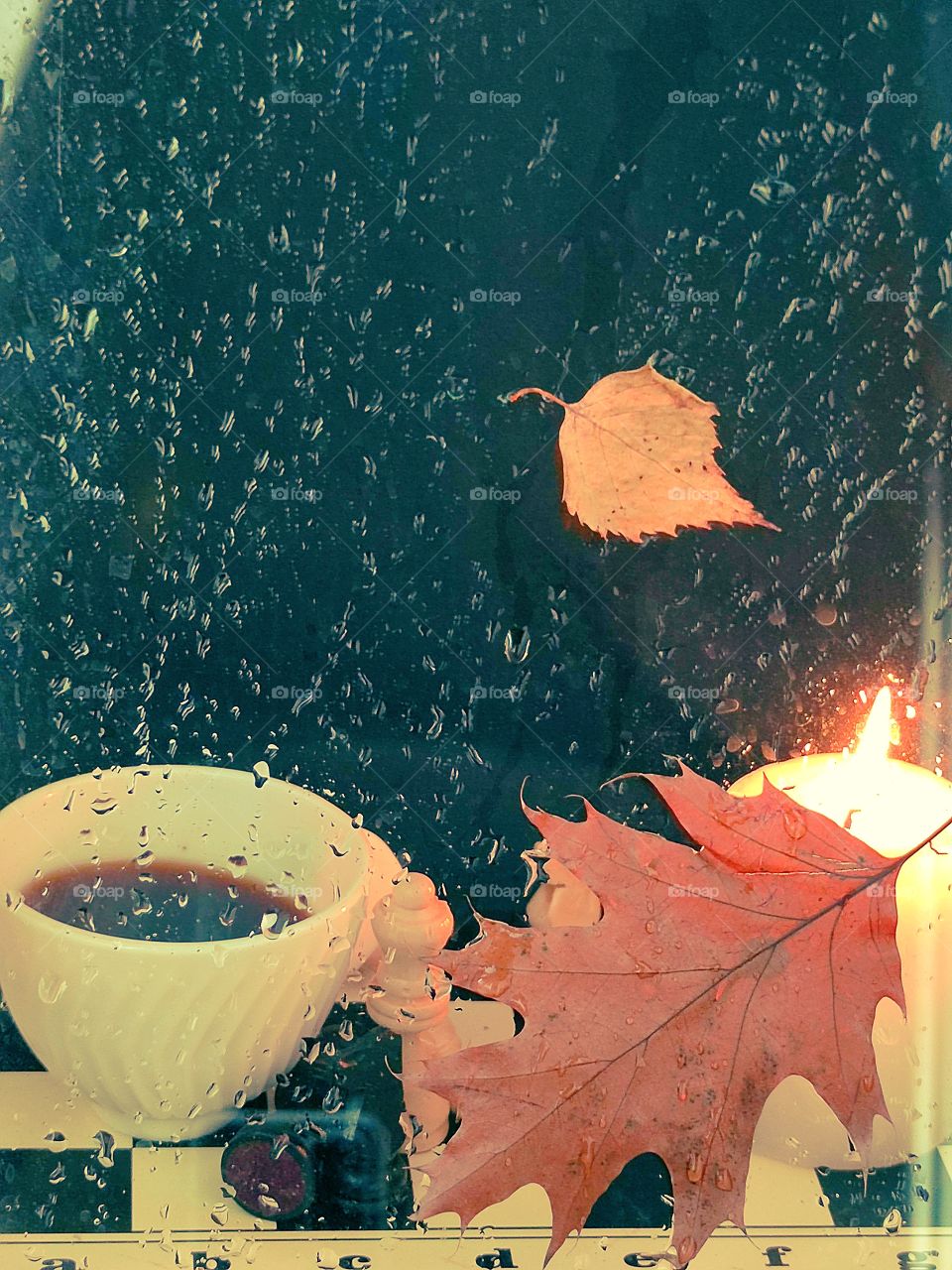 Rain.  Evening.  Glass in drops of water.  Behind the glass is a white cup with black coffee, which stands on a chessboard, a chess piece and a burning candle.  Autumn leaves stuck to the glass