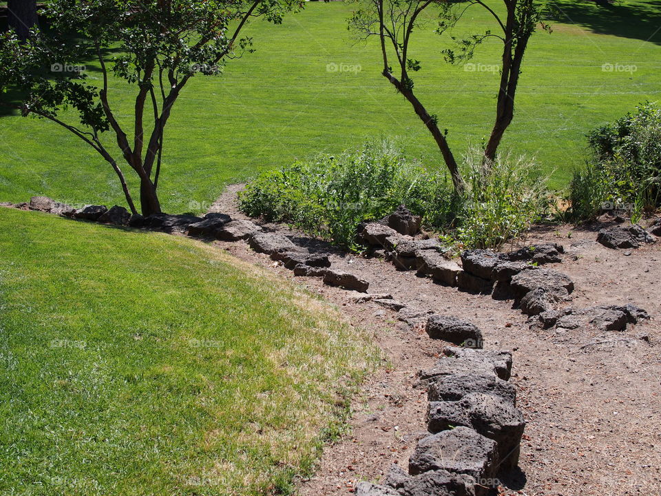 Multiple tiers with rock walls of different growth from grass to flowers and trees and a dirt path leading through in Pioneer Park in Bend in Central Oregon on a beautiful sunny summer day.