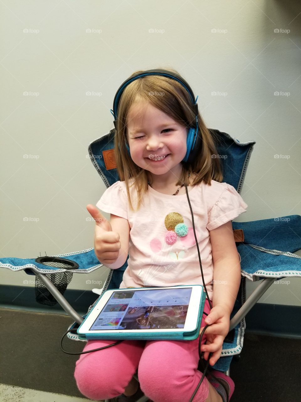 smiley little four year old girl giving thumbs up while on her ipad with headphones on