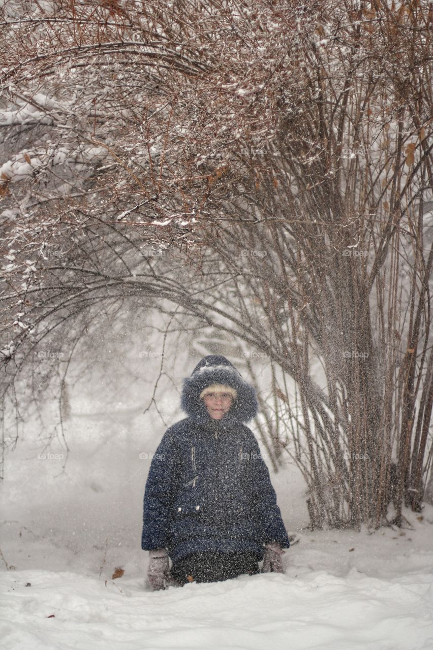 Girl plays in a snowdrift under a large bush