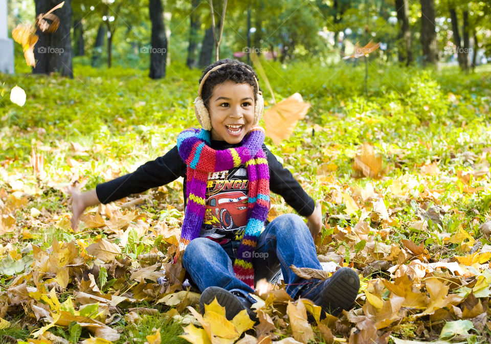 Boy sitting on dry maple leaves during autumn