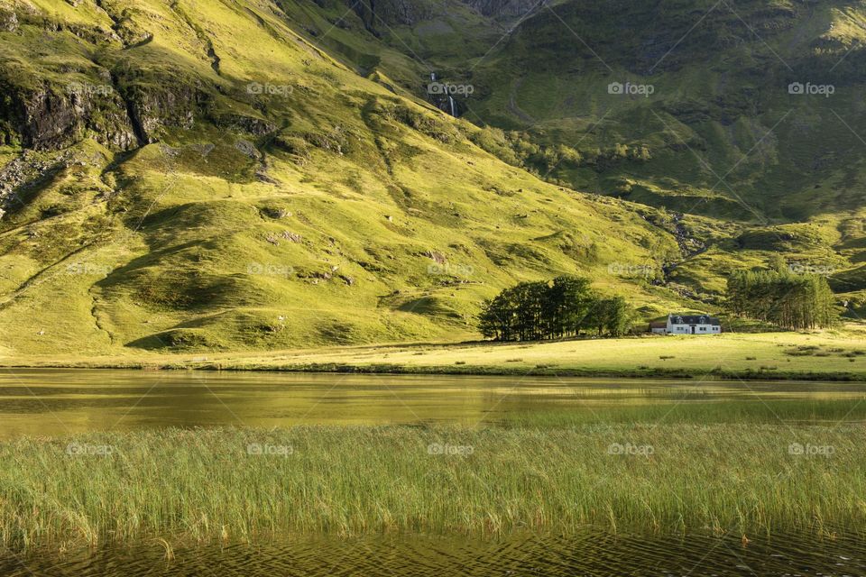 The tiny white cottage sits on a slight rise between a rugged mountain and a small loch in Glencoe, Scotland!