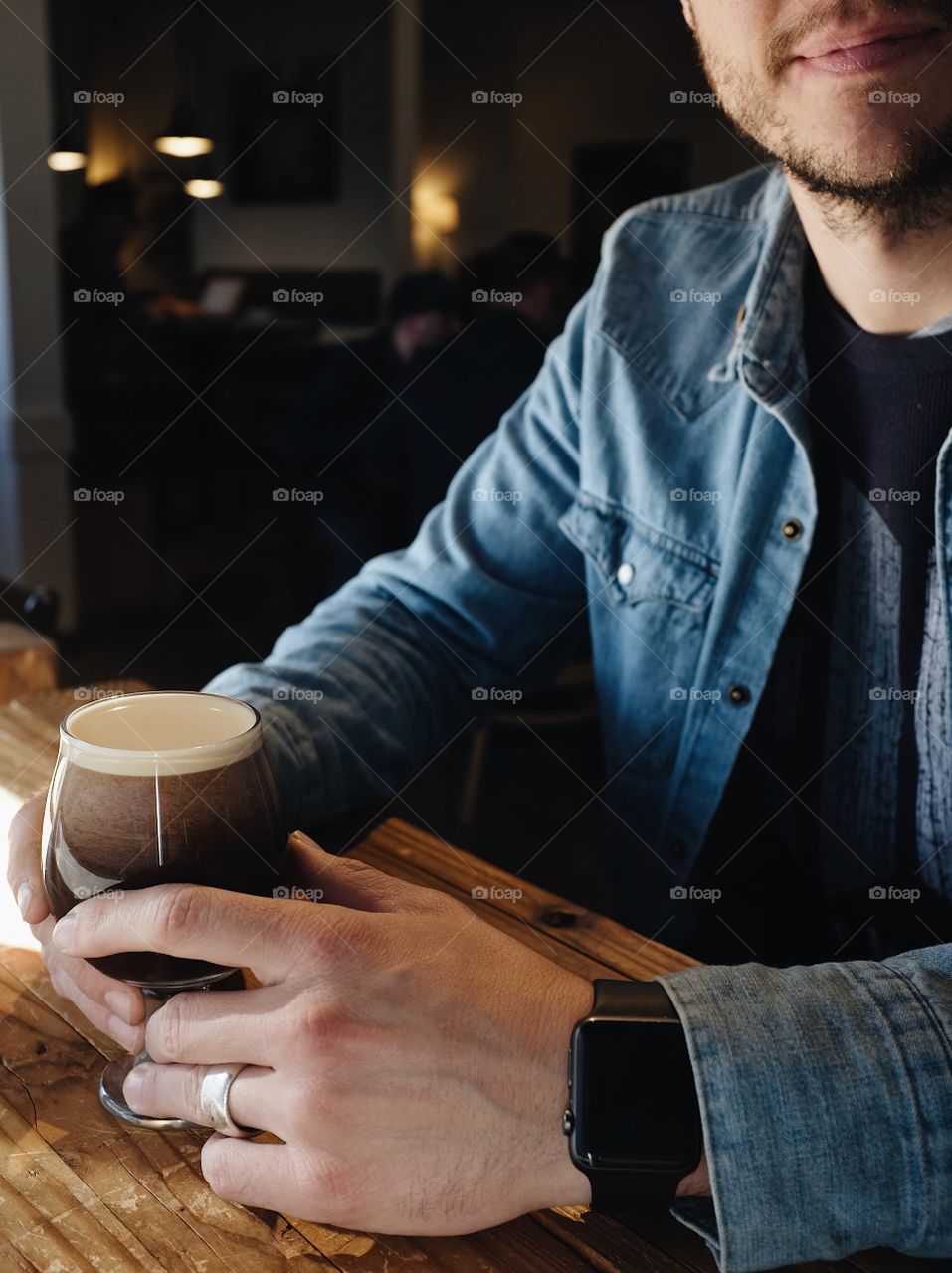 A married man sitting in a window enjoying a nitro cold brew coffee. He is wearing an Apple Watch, a Jean jacket, and a wedding ring on his finger.  
