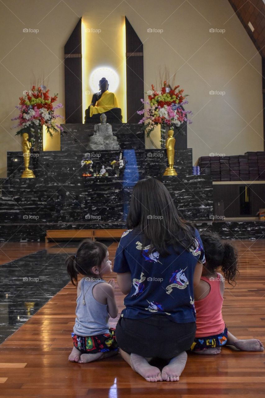 A young mother with two daughters praying to the Buddha for blessing.