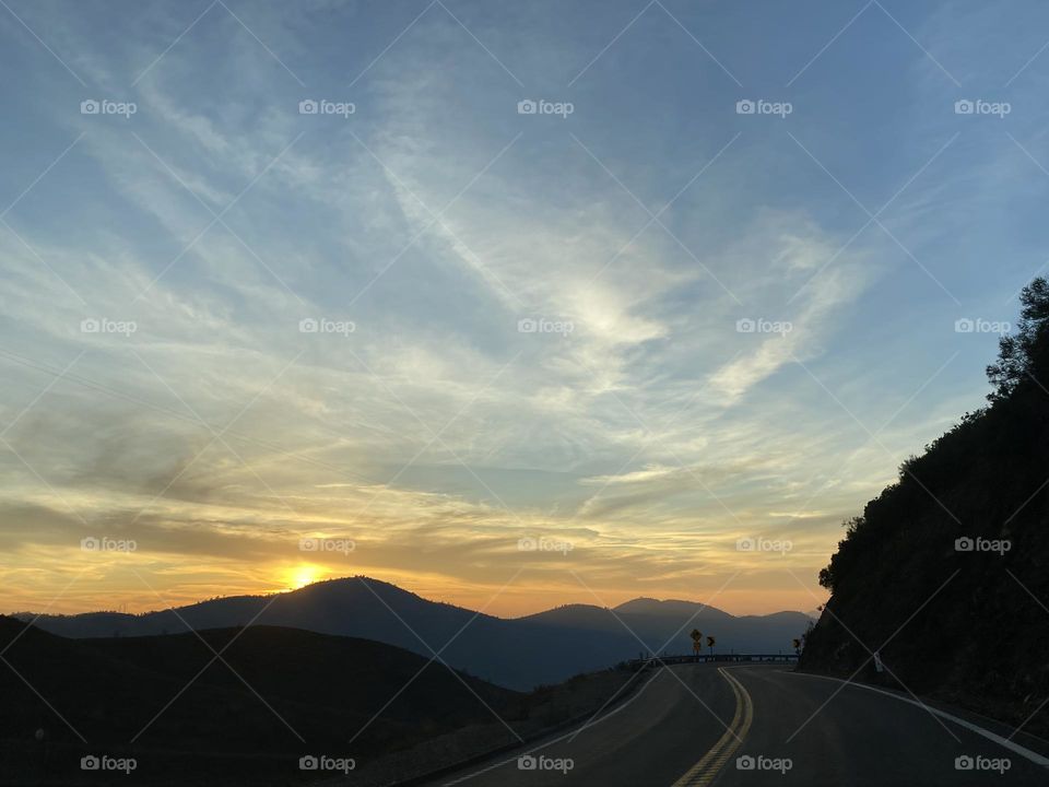 Distant mountains contrast an orange sunset sky on a mountain road