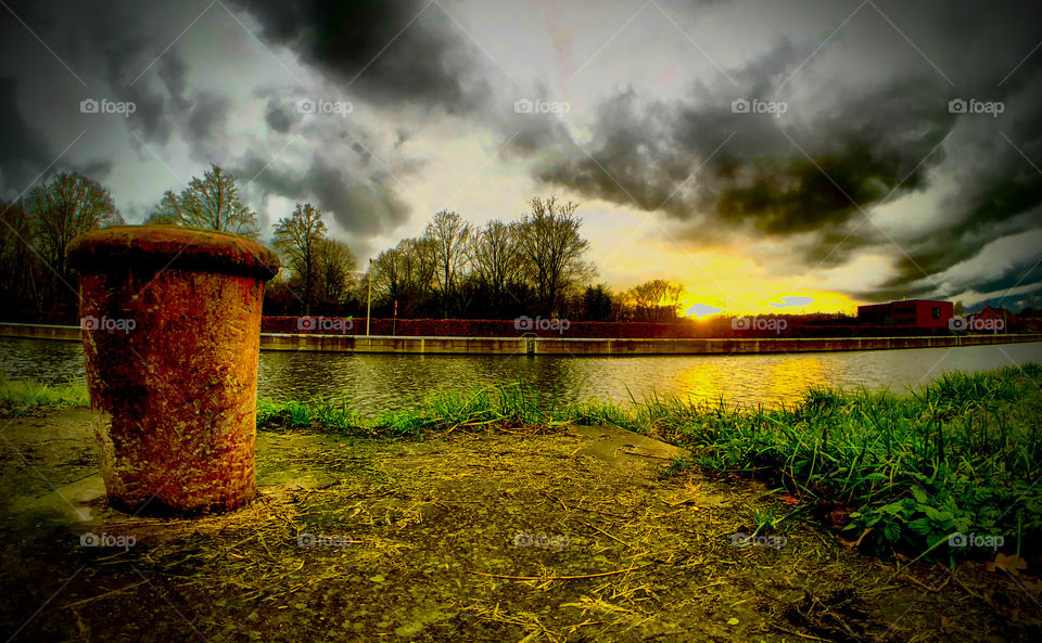 Rusty boulder on the woodland riverside under a stormy sunset sky