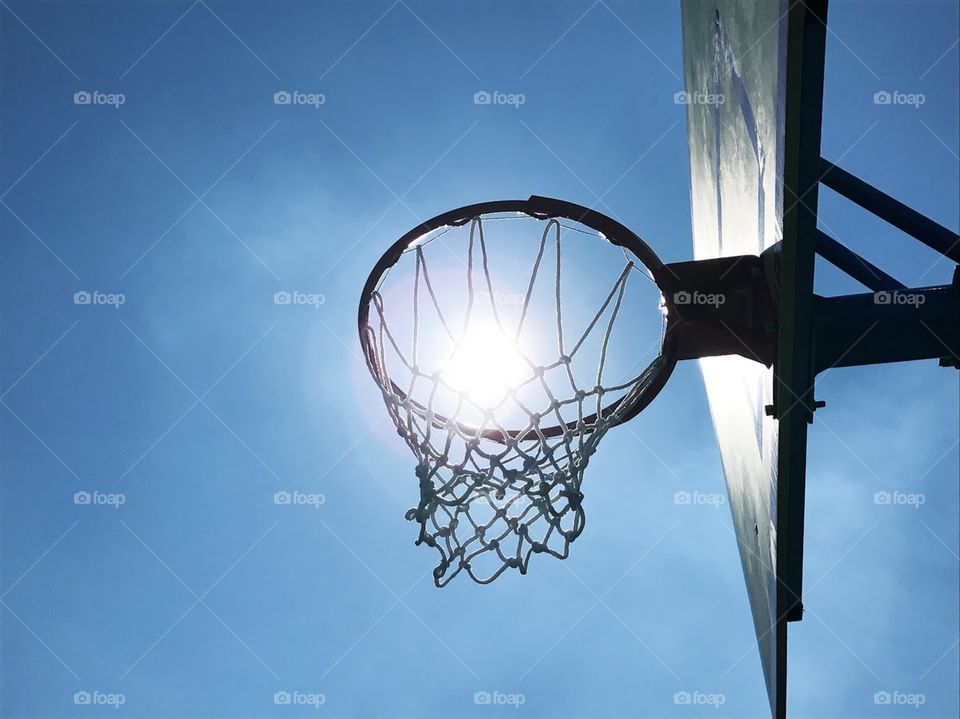Optical illusion of bright sun in basketball hoop against blue sky in the daytime 