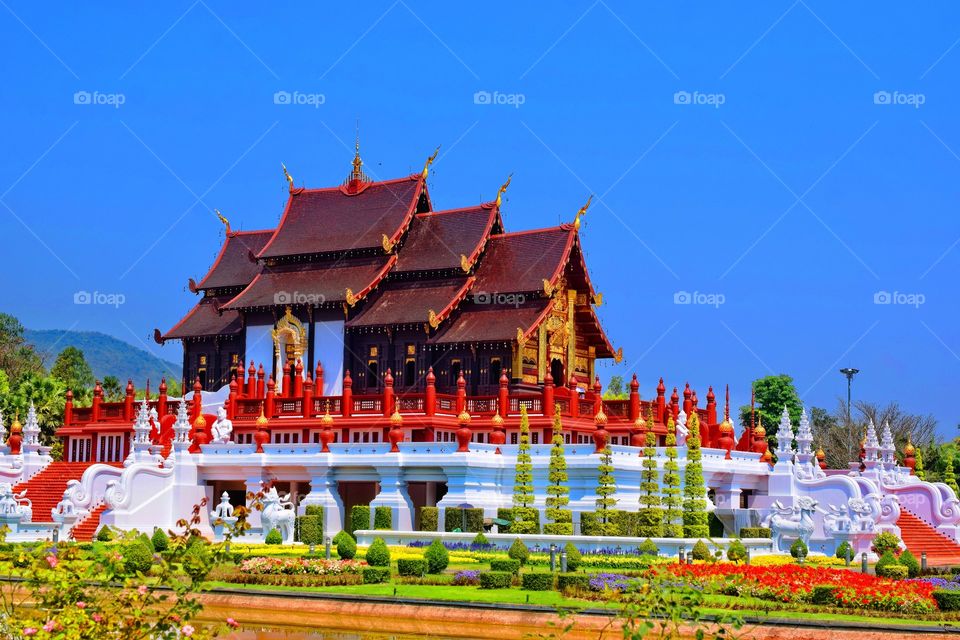 A beautiful, serene temple with vibrant red pillars, surrounded by a colorful garden of flowers located in the heart of The Royal Park Rajapruek in Chaingmai, Thailand