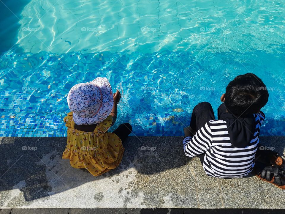 Kids sitting outside the swimming pool with their feet in water