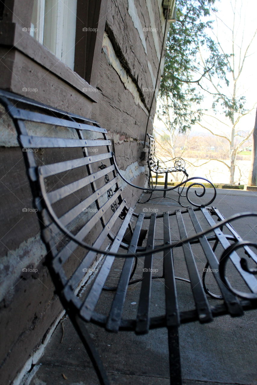 This is a picture of a metal bench sitting on the back porch of a log cabin home in the park in Point Pleasant, West Virginia.