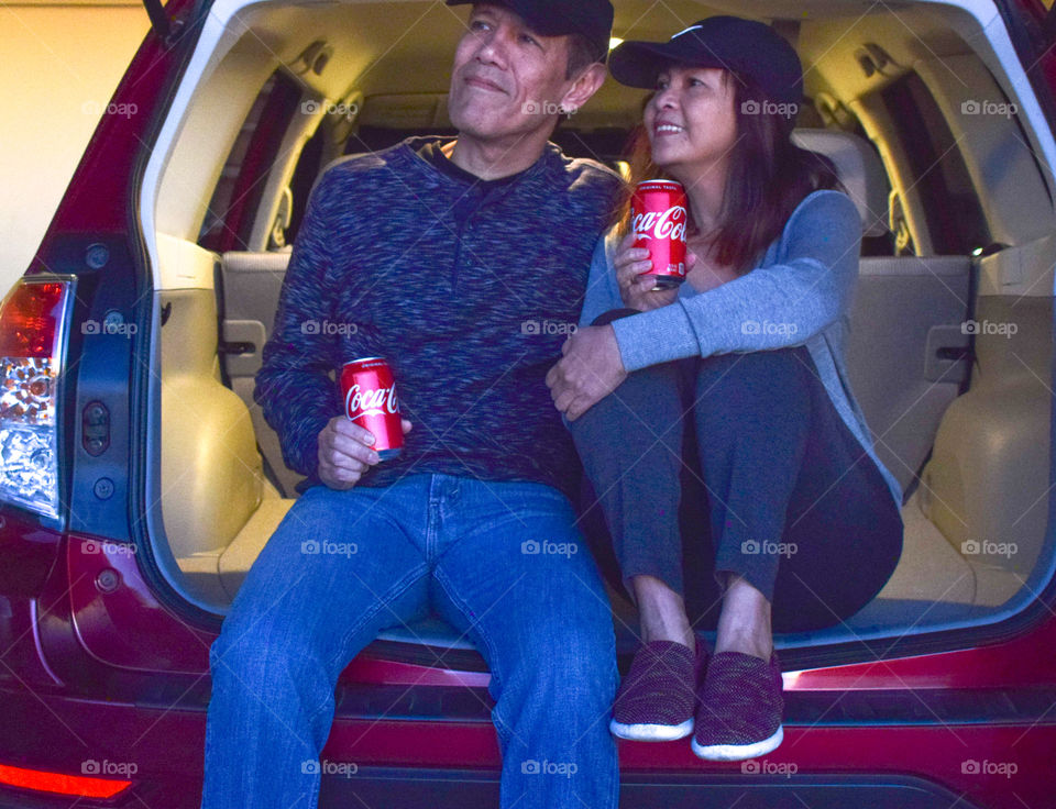 A couple relaxing in SUV hatchback with Coke 