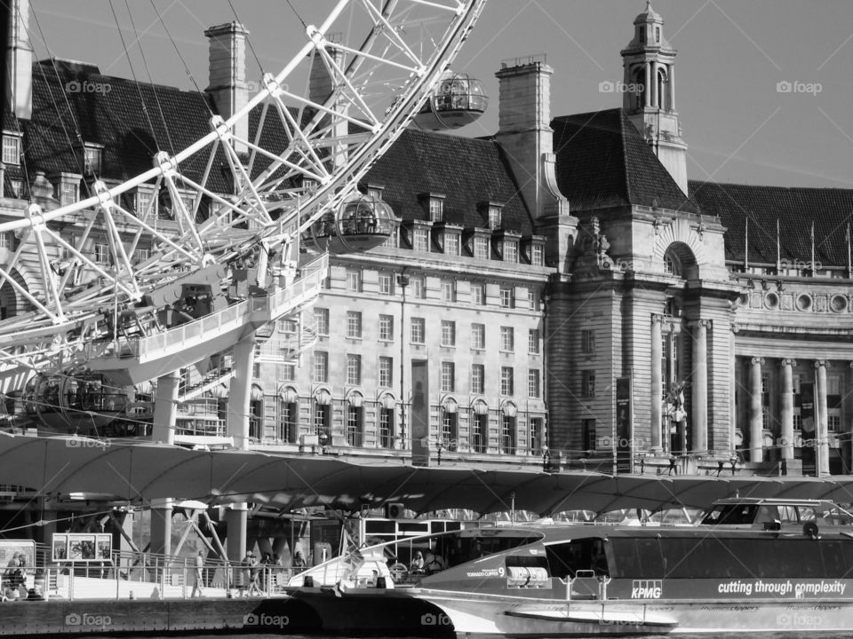 The London Eye towers above local historic buildings  and boats on the Thames River in London on a sunny summer day. 