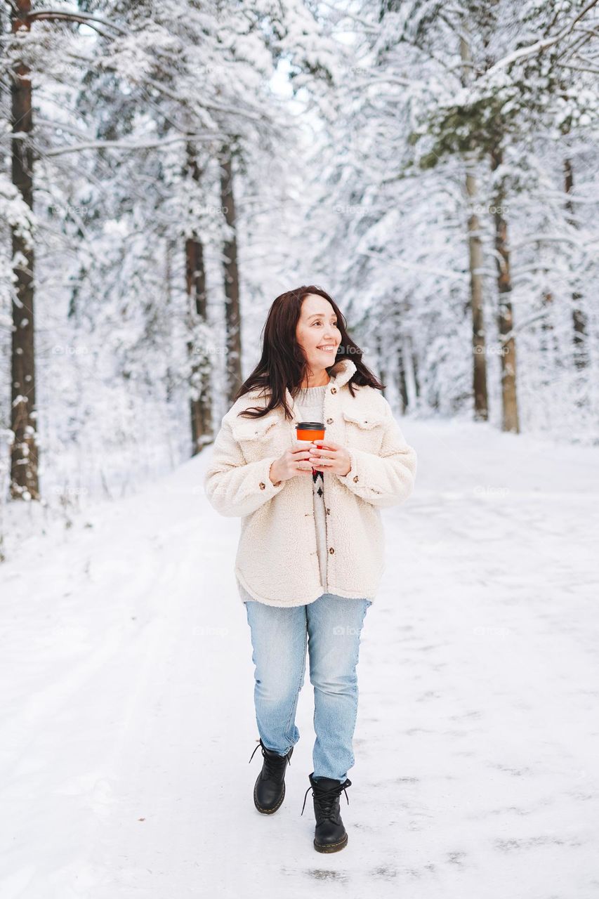 Young woman with coffee in black Dr. Martens boots in winter forest