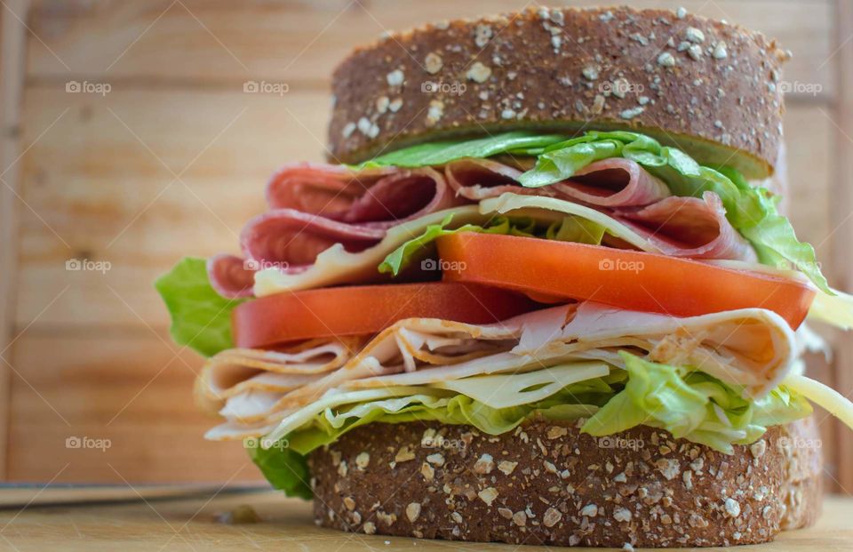 mixed meat deli sandwich with lettuce and tomatoes on grain bread served on wood table with wood background