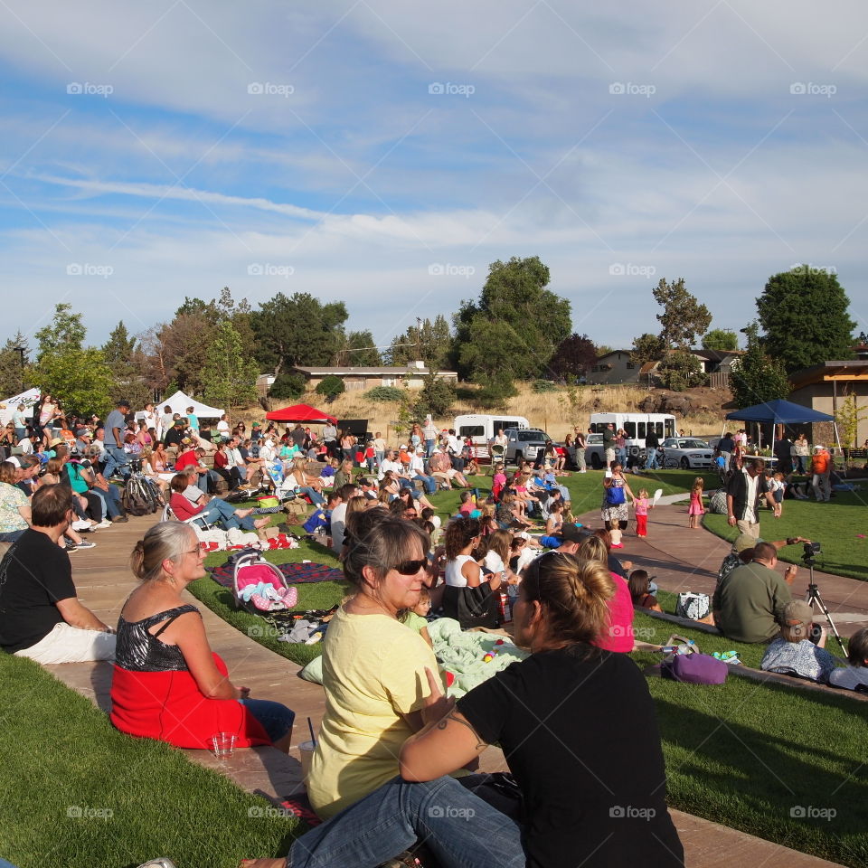 A crowd of people gathered for community music at the American Legion Park in Redmond in Central Oregon on a sunny summer evening. 