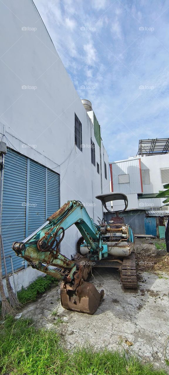 excavator in construction site with blue sky and white wall background