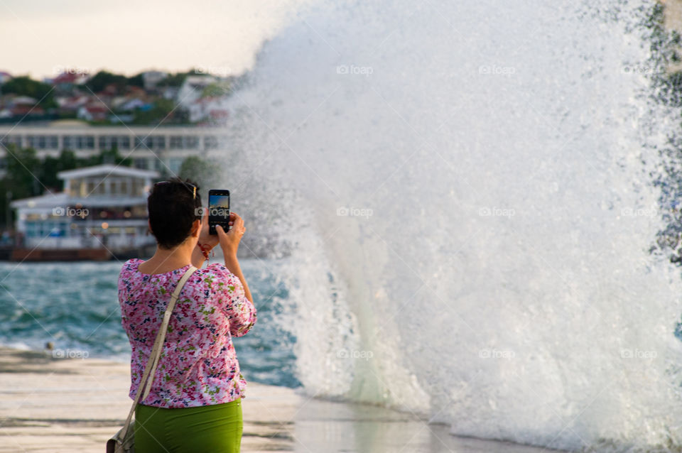 woman taking large splashes from the waves on the phone