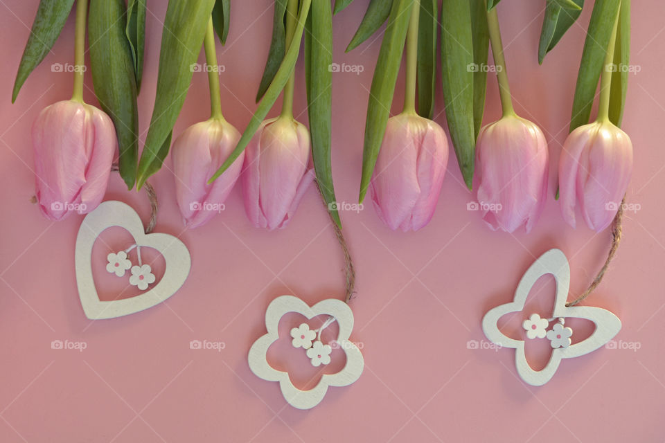 row of pink tulips on a pink wooden background with decorations made of wood.