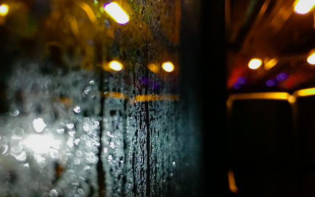 A wet glass window after hit by a rain at night, showing colorful light from outside