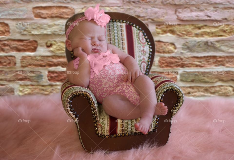 Newborn girl posing in a doll chair