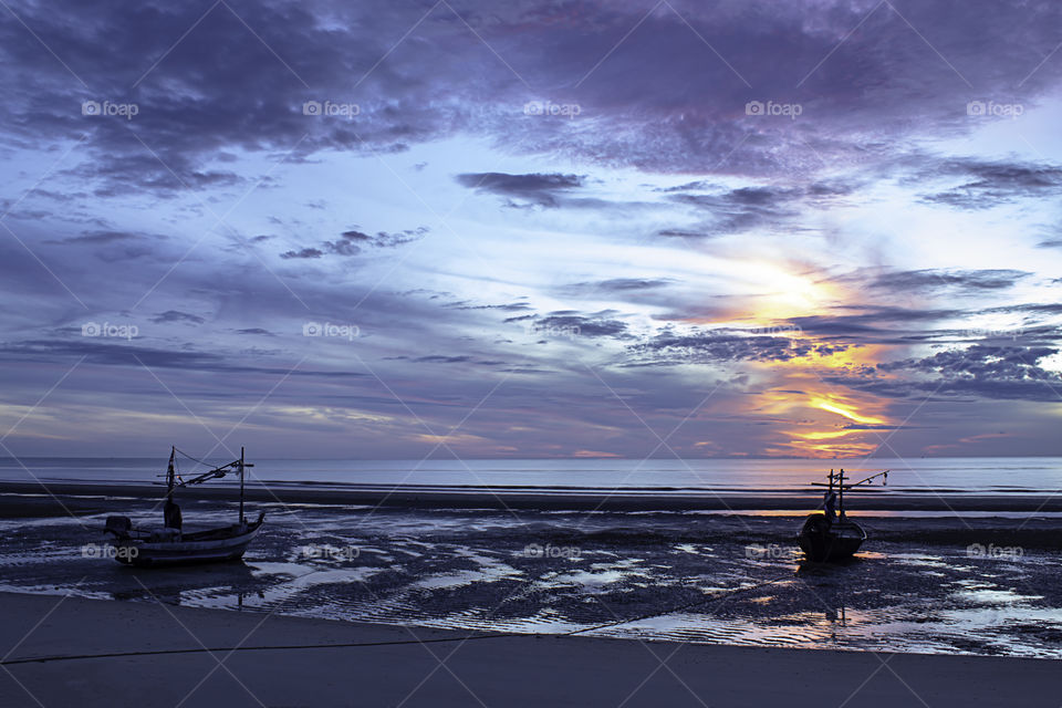 The morning sun light in the sea and the boat on the beach.