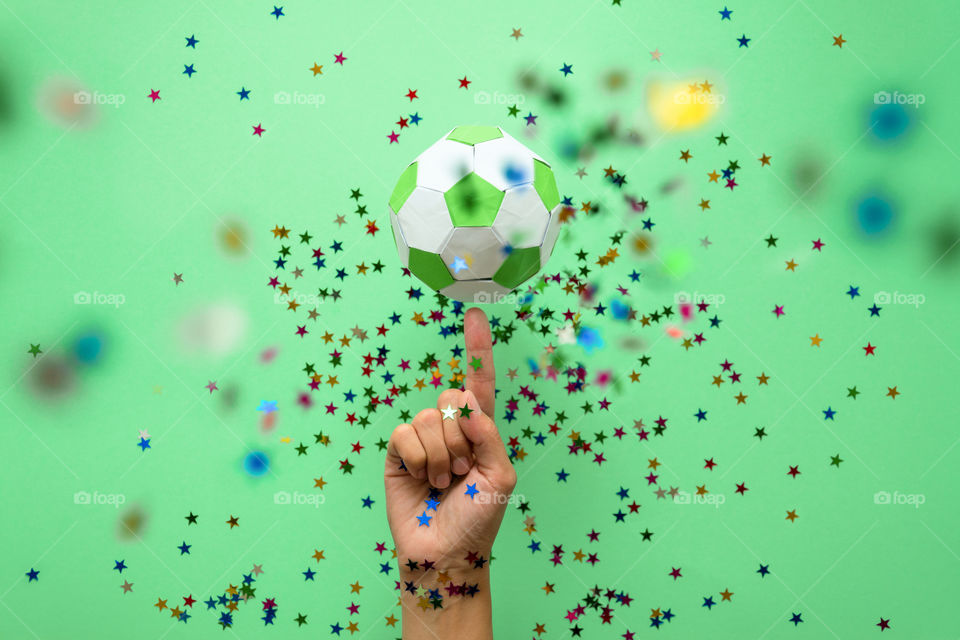Hand spinning paper soccer ball on green background. Origami. Paper craft. Soccer game concept.