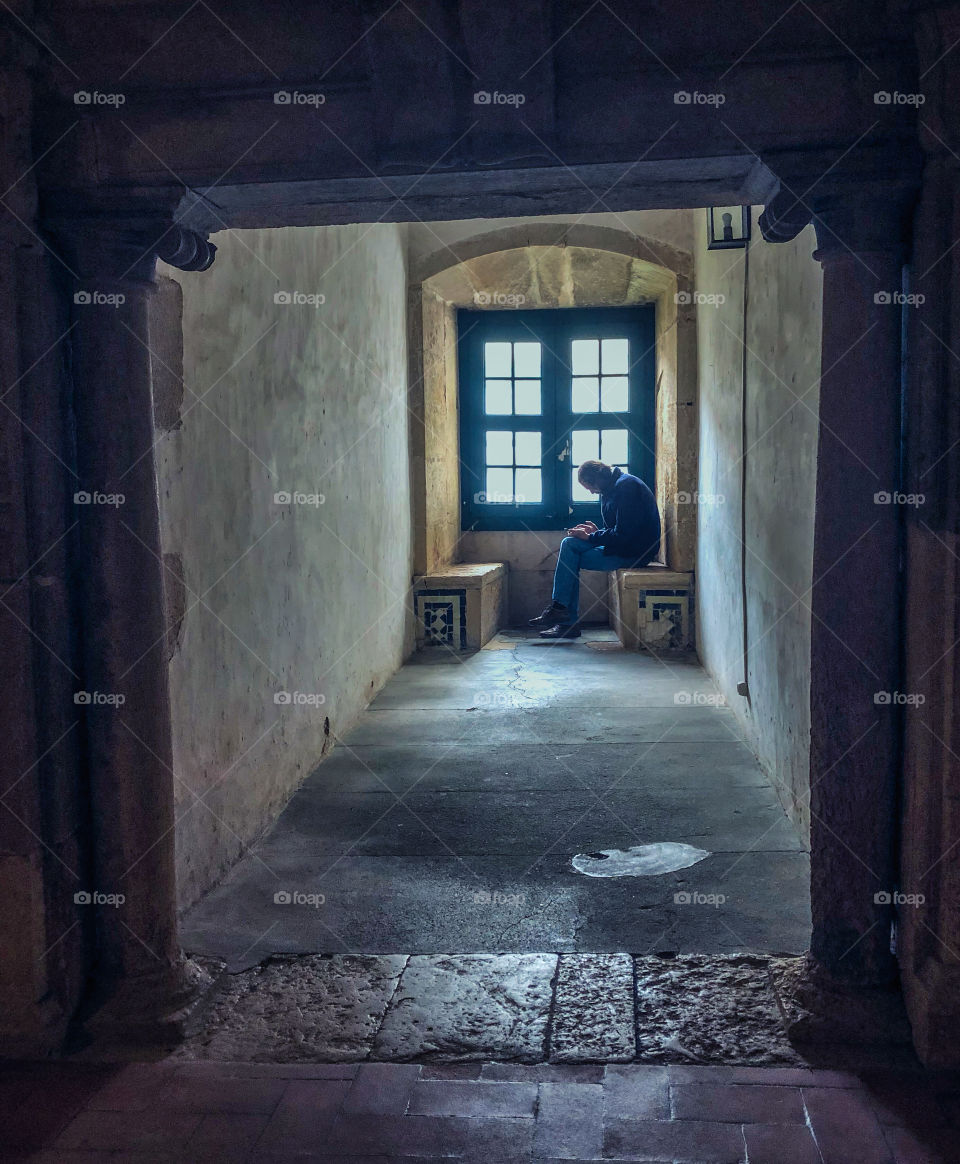 As a monk in years gone by may have huddled over his prayer book, this tourist looks at his phone in a quiet corner of The Convent of Christ, Tomar, Portugal