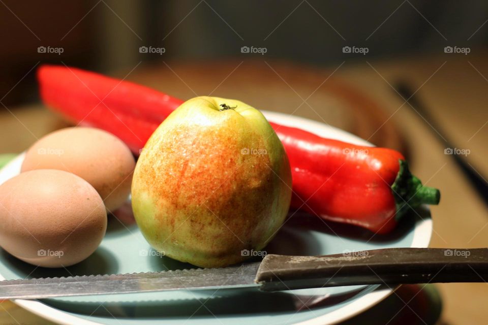 Apple, red pepper, eggs and knife on a plate