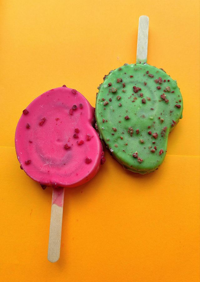 Summer.  Time to cool off.  On an orange background are two ice creams: red raspberry with raspberry pieces and green kiwi with chocolate pieces.  Contrast of colors and taste