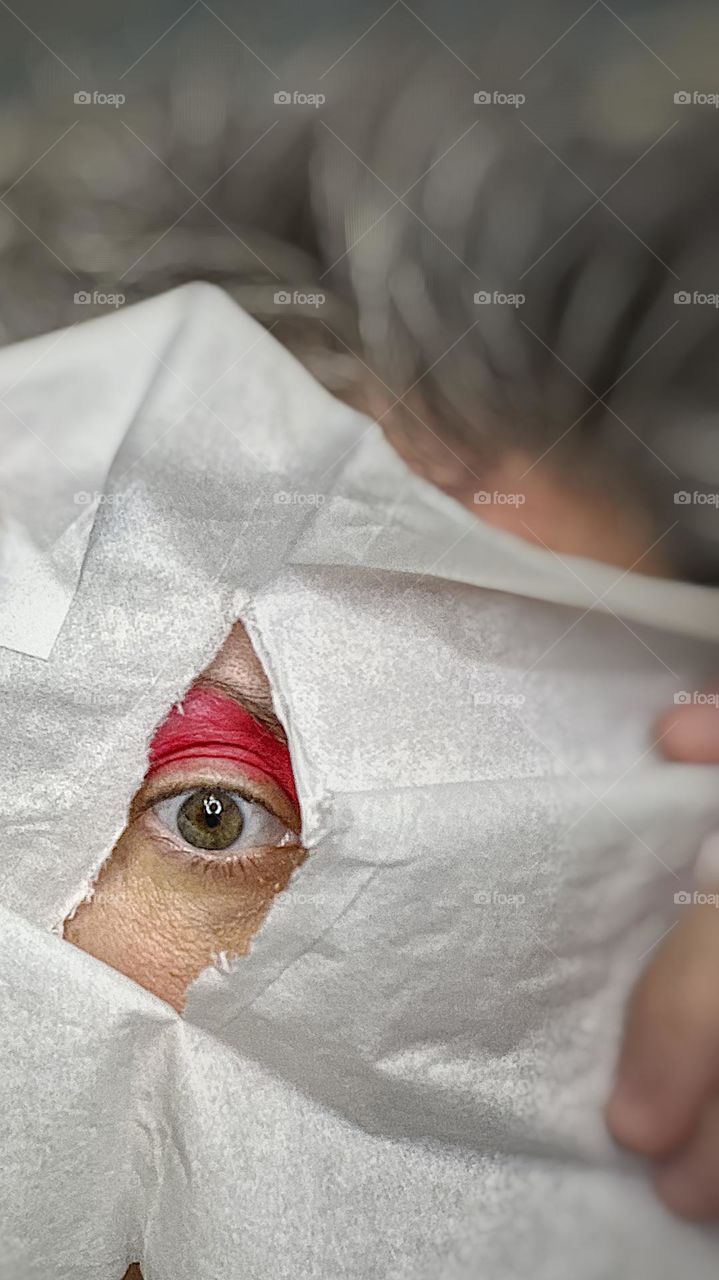 Woman’s eye peeking out from a torn cloth, bright colored eye shadow on woman’s eye, eyes and eye shadow, bright pink, woman peers into camera lens, looking at you, peek a boo, edgy and unique makeup advertising