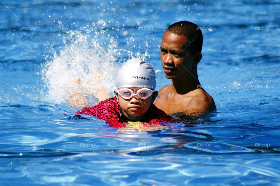 young kid learns how to swim with the help of a swimming coach