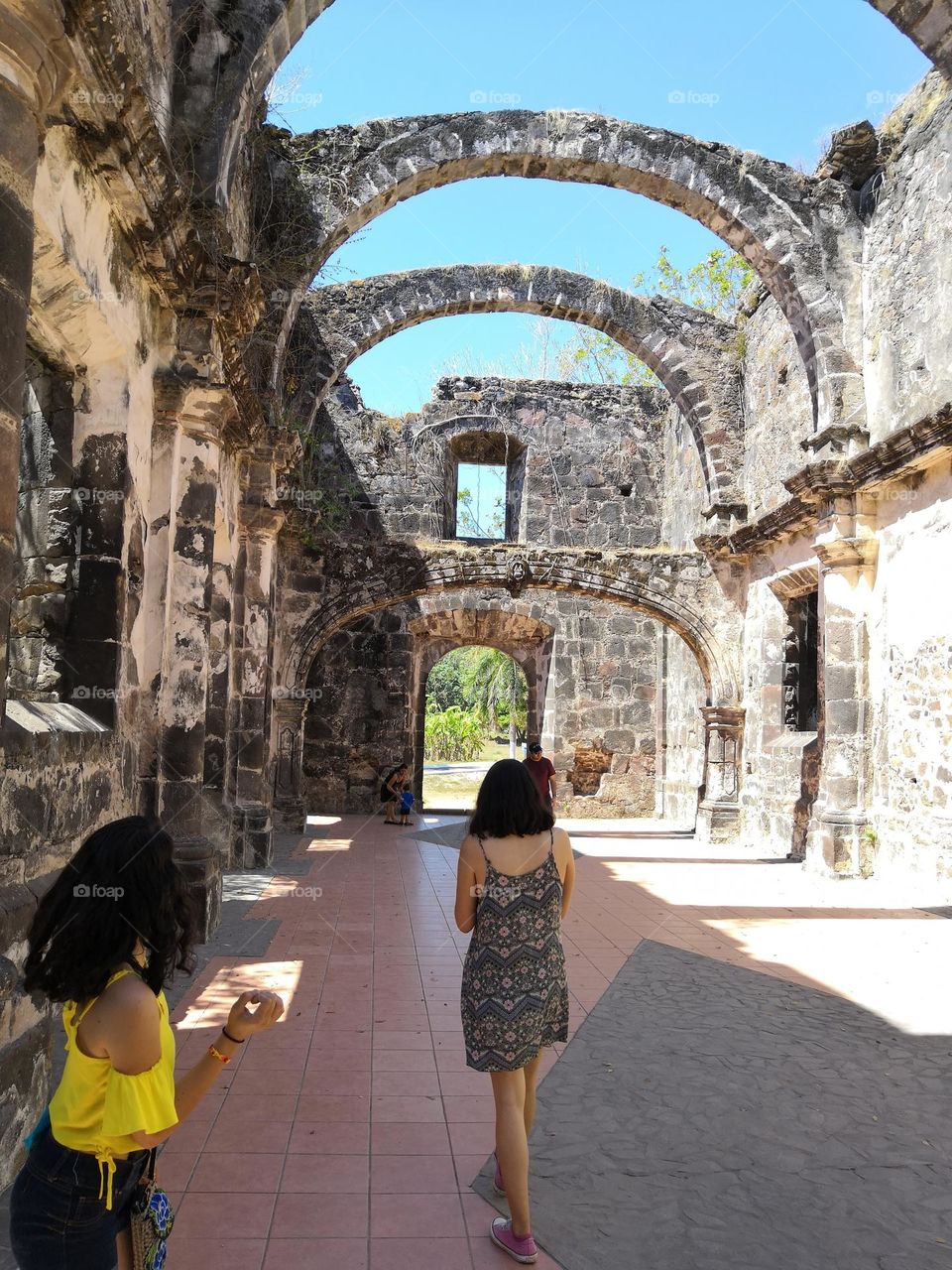 Tourists appreciating an ancient temple ruins with large arches above with the sky as background.