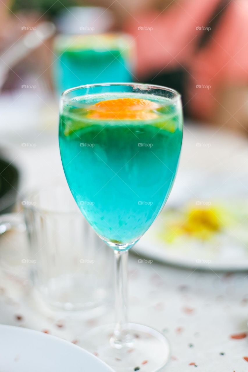 A beautiful blue summer drink with a slice of orange in a glass of stomt on the table, vtd side close-up.