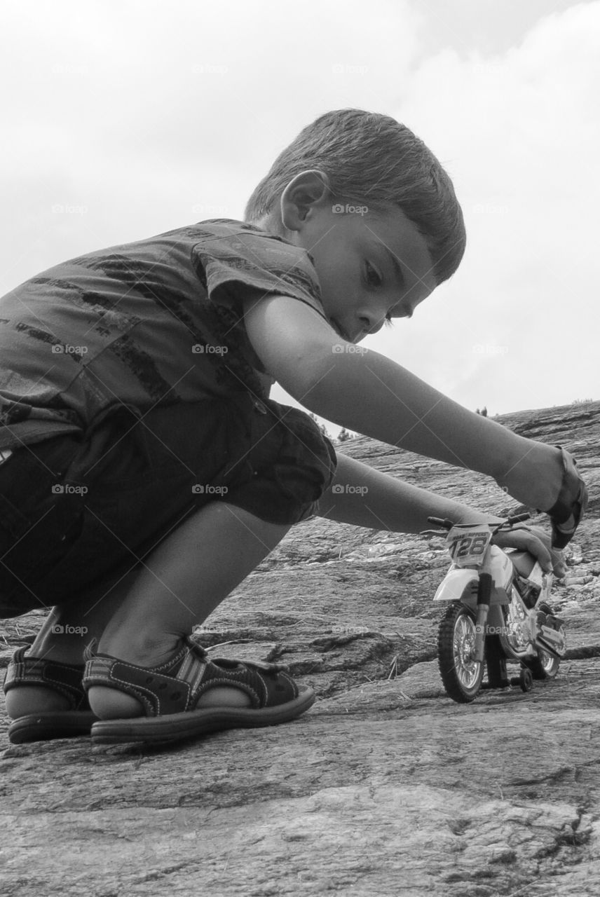 Boys and Bikes. A young boy playing outside with his toy dirt bike on a big rock