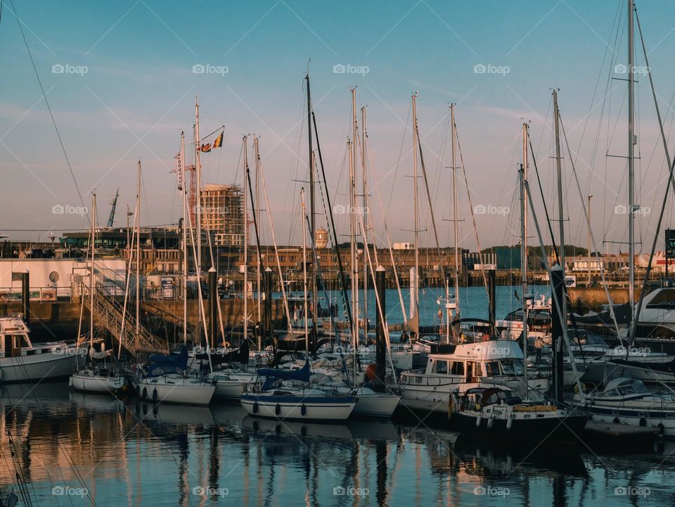 Many yachts and boats moored on the North Sea pier in the city of Oostende in Belgium in the evening and sunset time, close-up side view.