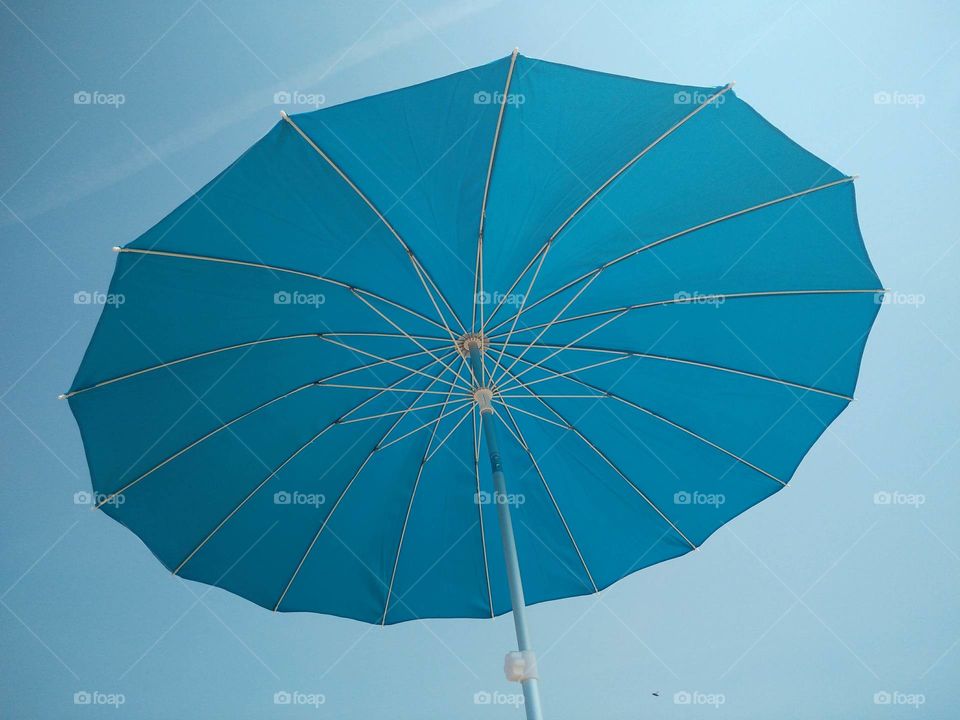 A portrait of a blue umbrella in a blue sky.  it almost fades away in the blue of the sky.