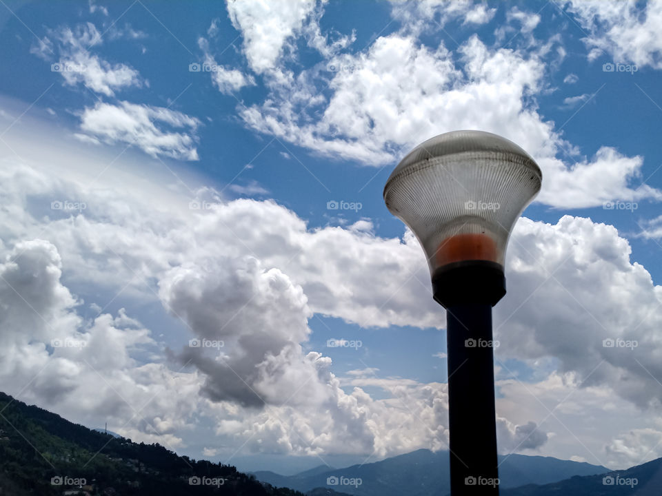 photo of a street light. lamp post. light pole. in the background with full of clouds and cloudy sky. blue sky. clean and clear weather.