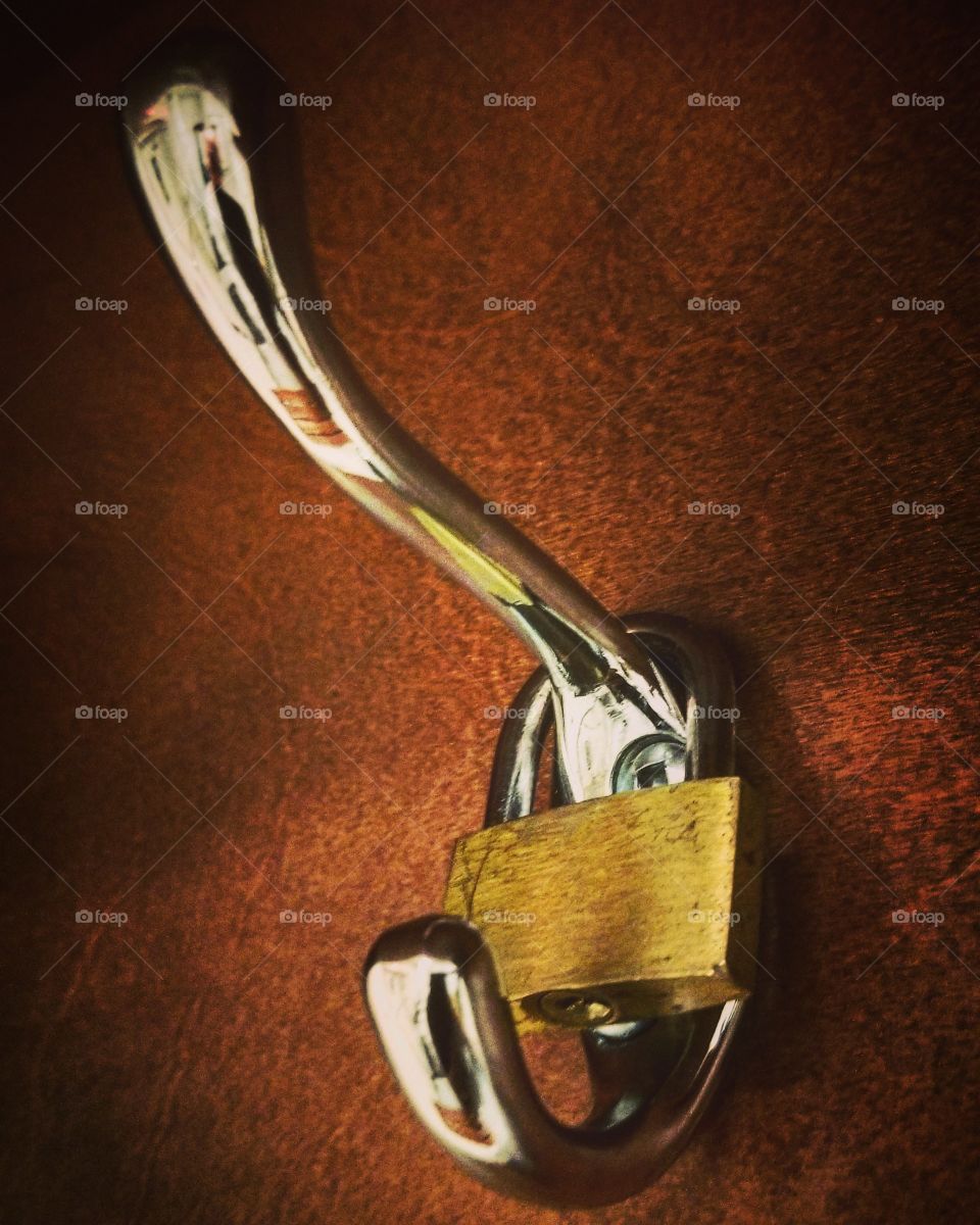 Lock on a coat hook, brass colored lock on a polished sliver colored hook, reddish brown wood textured background.