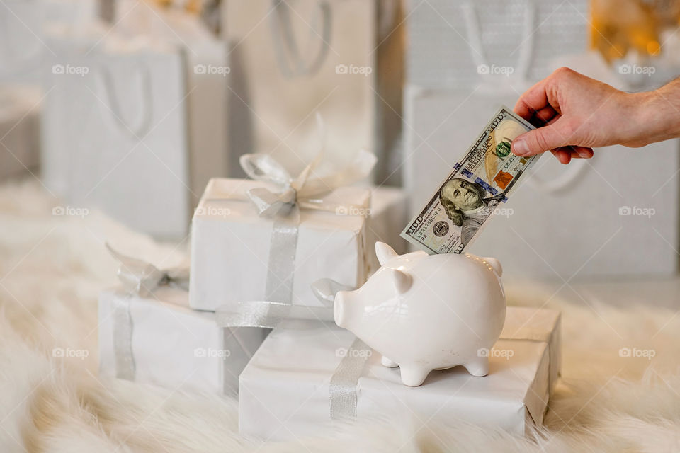piggy bank with 100 dollars banknote in festive New Year atmosphere of scenery. Magical bokeh with Christmas tree and bright lights.